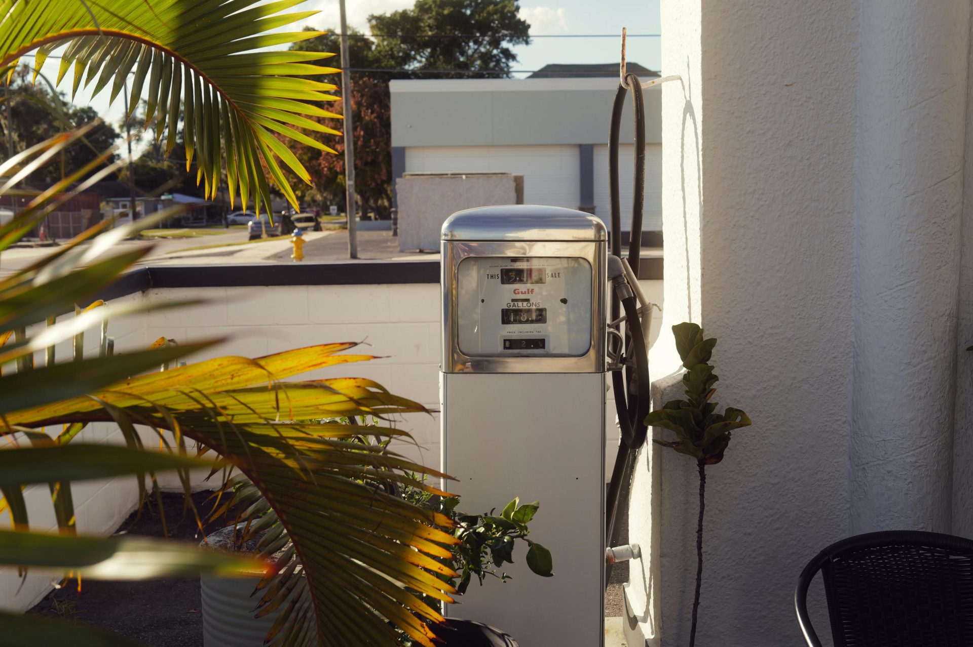 Eine von Palmenblättern umgebene, historische Zapfsäule fängt bei Tageslicht eine nostalgische urbane Atmosphäre ein.