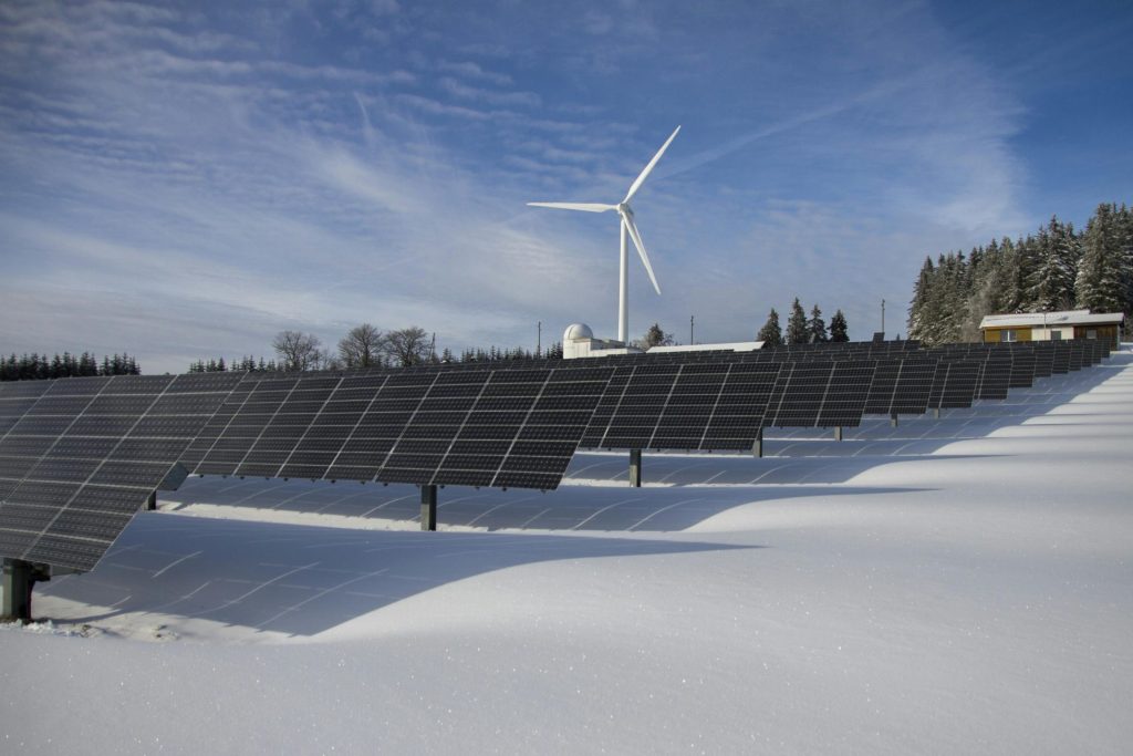 Solarpaneele und Windkraftanlage in einer verschneiten Landschaft, die erneuerbare Energiequellen demonstrieren.